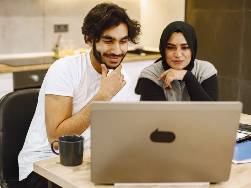 beautiful-young-couple-using-laptop-writing-notebook-sitting-kitchen-home-arab-girl-wearing-black-hidjab_1157-48423